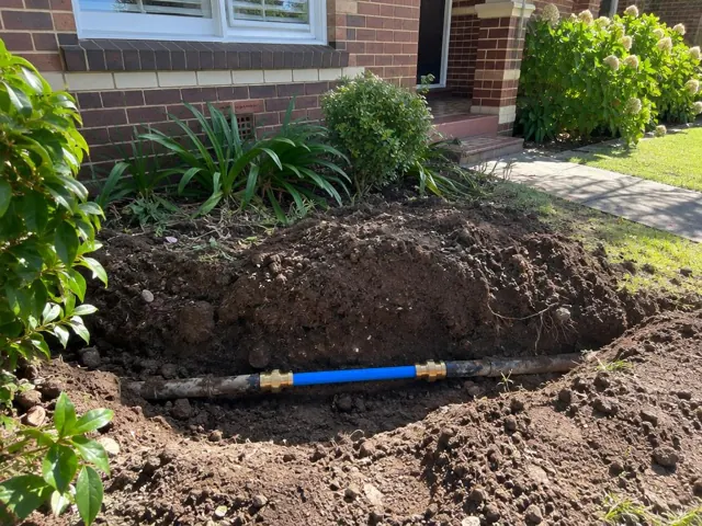 Exposed repaired water pipe in a front garden trench beside a brick house in Killara