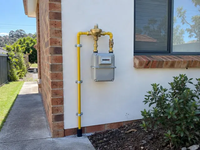 Yellow gas meter and pipework mounted on an exterior brick and render wall beside a window in St Ives